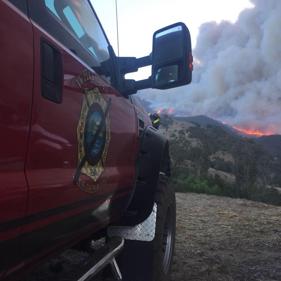Red and black brush truck parked with fire on mountain in the distance